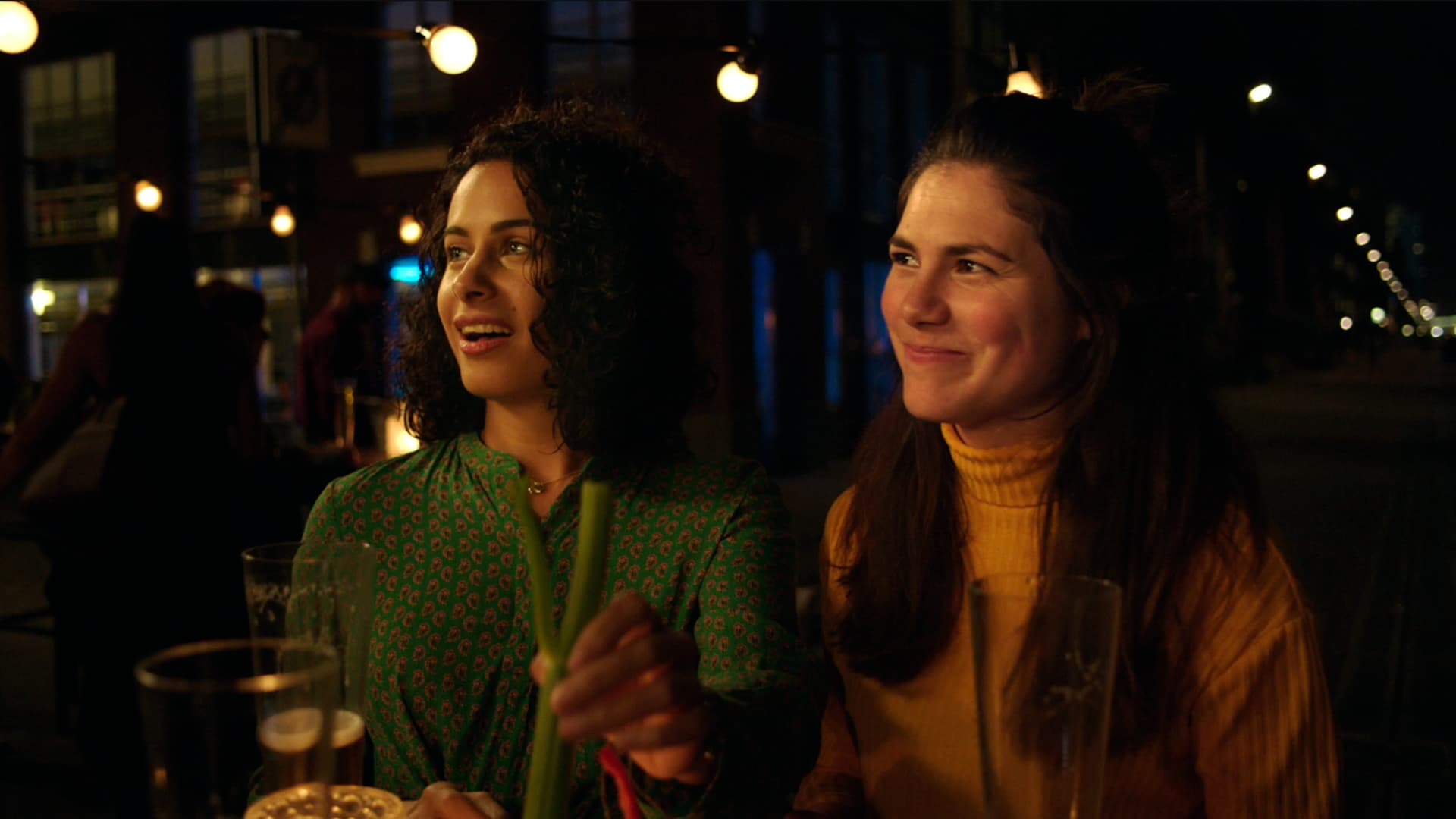 Two women are sitting side by side on a restaurant table, at night.