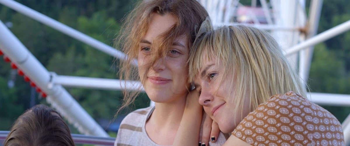 Two women are on a Ferris wheel, one of them has her head on the other's shoulder. They are both smiling.