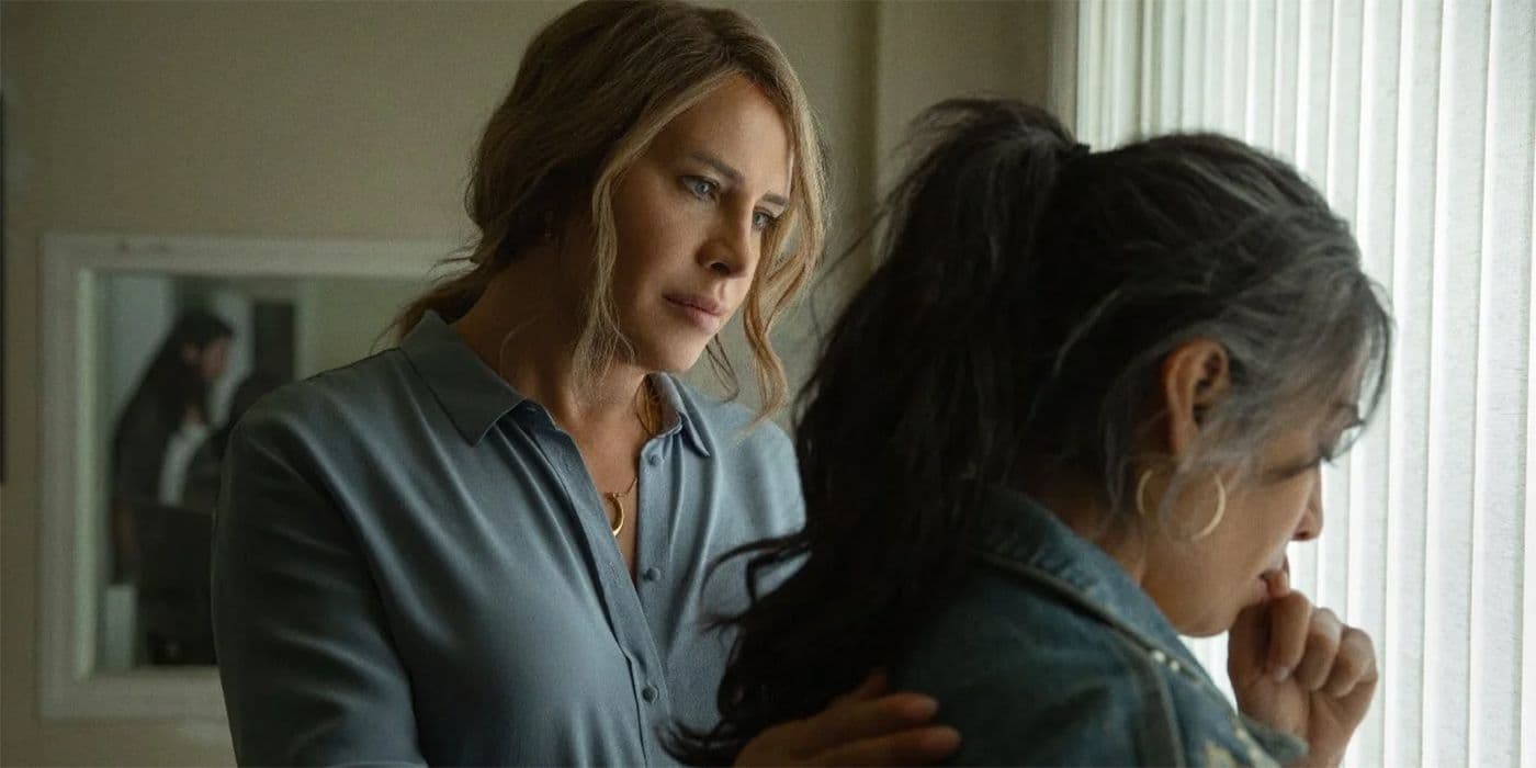 A woman is conforting another women next to a window.